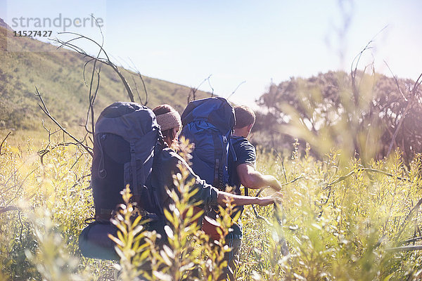 Junges Paar mit Rucksäcken beim Wandern im sonnigen  hohen Grasfeld