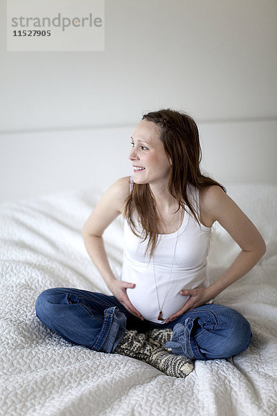 Lächelnde schwangere Frau auf dem Bett