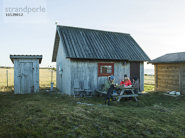 Menschen beim Essen vor einem Holzhaus