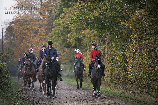 Eine Reihe oder Gruppe von Reitern auf Vollblutpferden  die einen Weg entlang reiten. Rennpferde im Training. Routineübung.