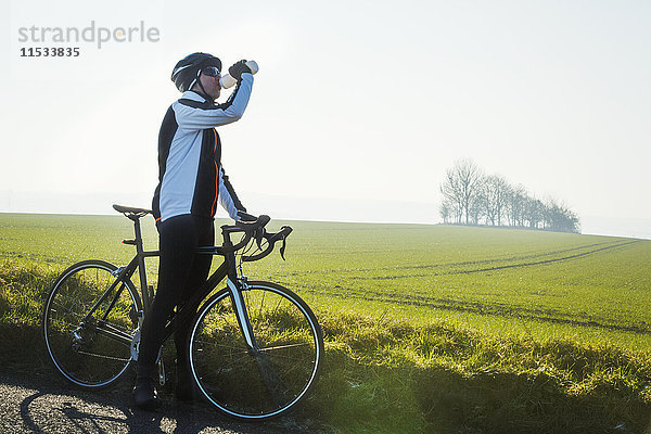 Ein Radfahrer am Straßenrand  der eine Pause macht und aus seiner Wasserflasche trinkt.