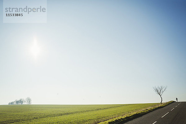 Ein Mann mit einem Rennrad auf einer Landstraße  Silhouette auf der Stirn eines Hügels. Verschwindet in der Ferne.