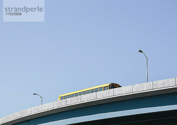 Ein gelber Schulbus fährt über eine erhöhte Fahrbahn gegen einen blauen Himmel.