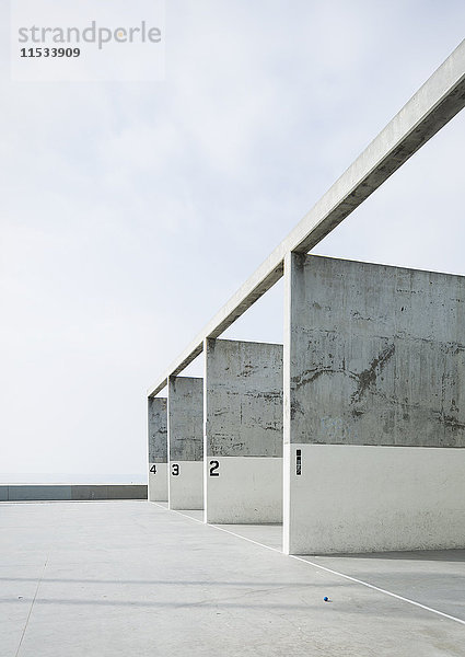 Nummerierte Betonpfeiler in einem Handballfeld vor blauem Himmel.