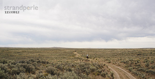 Ein Fahrer auf einem Feldweg  der durch eine flache  ländliche Landschaft fährt.