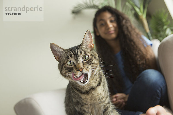 Ein Mädchen sitzt auf einem Sofa mit einer Hauskatze.