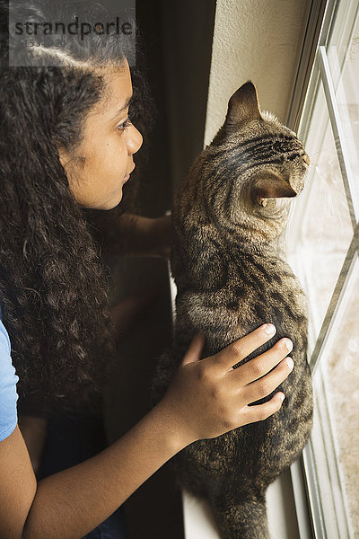 Ein junges Mädchen mit einer Katze am Fenster.