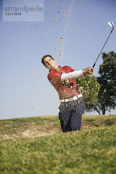 Golfer  der einen Golfball aus einem Sandbunker eines Golfplatzes schlägt.
