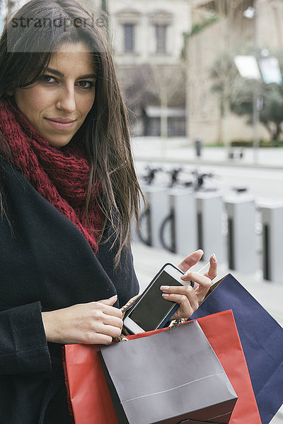 Spanien  Portrait einer jungen Frau mit Smartphone und Einkaufstaschen