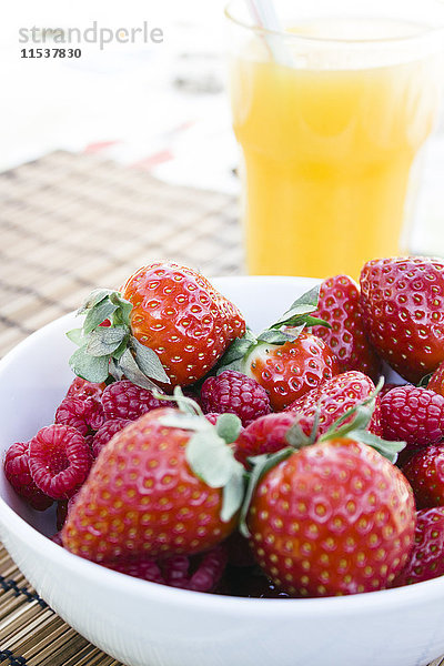 Erdbeeren und Himbeeren in einer Schüssel und einem Glas Orangensaft