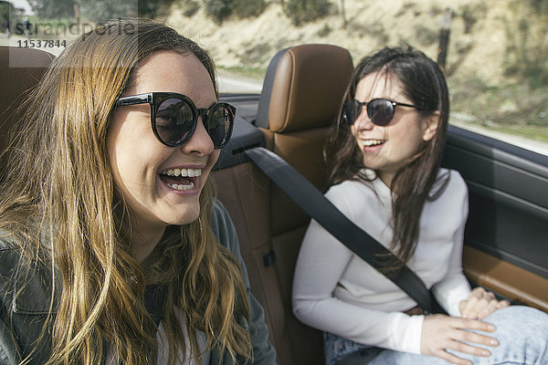 Zwei Frauen mit Sonnenbrille lachend in einem Cabriolet