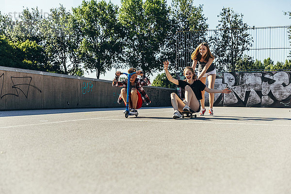 Drei verspielte Teenager-Freunde mit Roller und Skateboard
