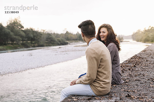 Italien  Belluno  junges Paar vor einem Fluss sitzend