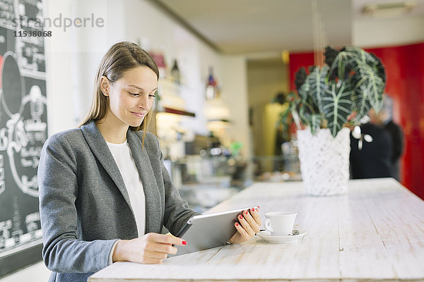 Junge Frau in einem Café mit Blick auf digitales Tablett