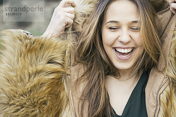 Porträt einer lachenden Frau beim Anziehen der Kapuze einer Pelzjacke