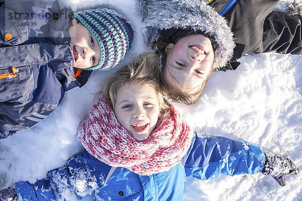 Porträt von drei auf Schnee liegenden Kindern