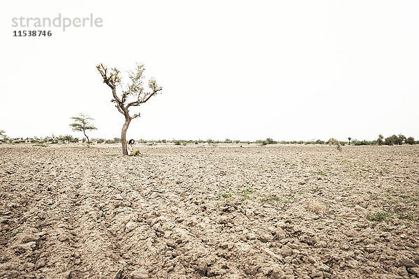 Mann sitzt allein unter einem Baum in der Wüste.