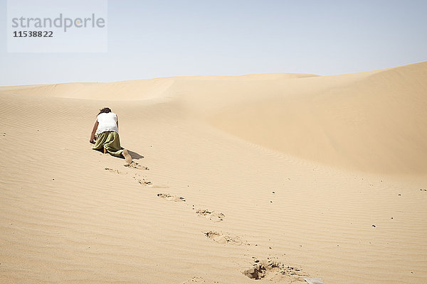 Ein Mann  der allein in der Wüste auf allen Vieren kriecht.