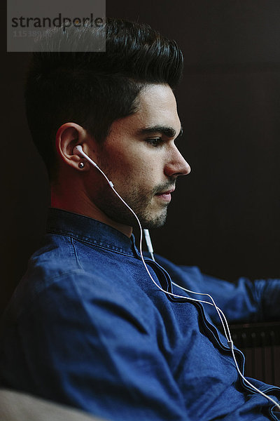 Profil eines jungen Mannes  der Musik mit Kopfhörern vor schwarzem Hintergrund hört.