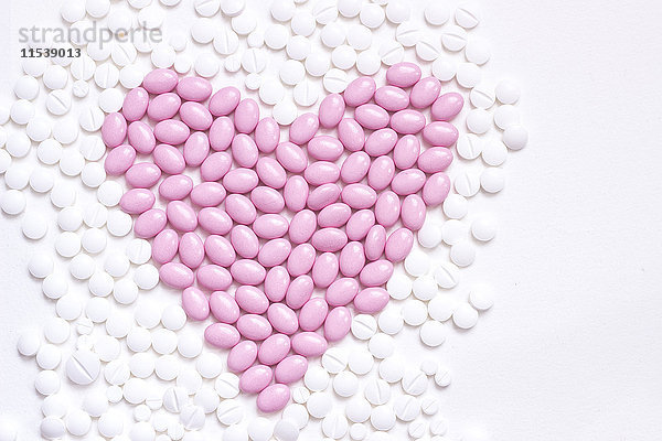 Pinkes Herz in Form von Pillen zwischen weißen Tabletten
