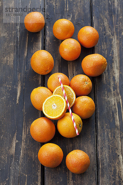 Ganze und geschnittene Orangen und ein Trinkhalm auf Holz
