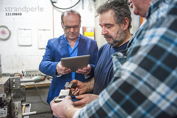 Drei Männer mit digitalem Tablett untersuchen Werkstücke