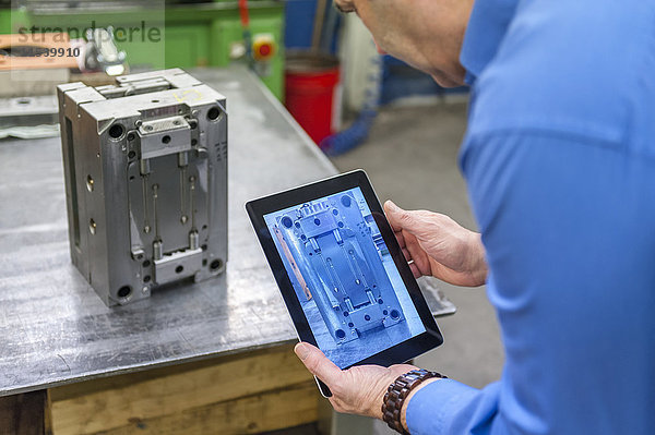 Mann mit digitalem Tablett zur Untersuchung von Metallwerkstücken
