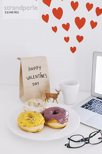 Stilleben mit Laptop  Donuts  Valentinstagsgeschenk und Herzen an der Wand