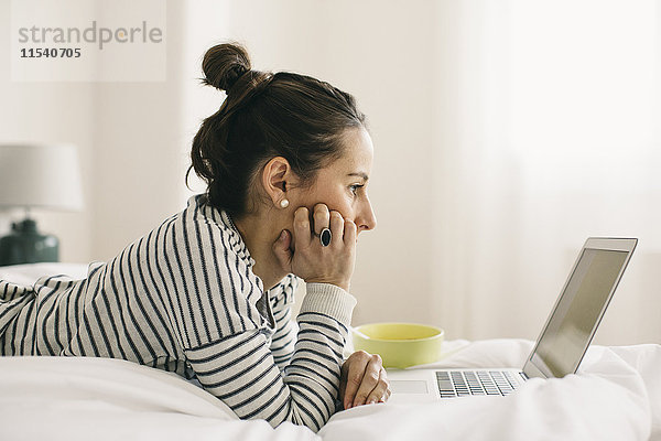 Entspannte Frau im Bett liegend mit Laptop