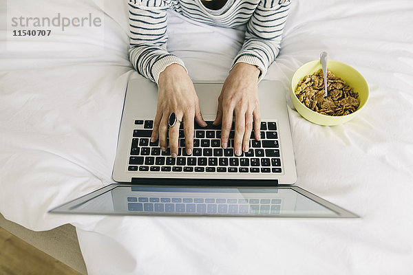 Frau im Bett mit Laptop und Müslischale