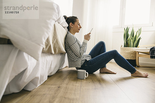 Entspannte Frau im Schlafzimmer mit Blick auf das Handy