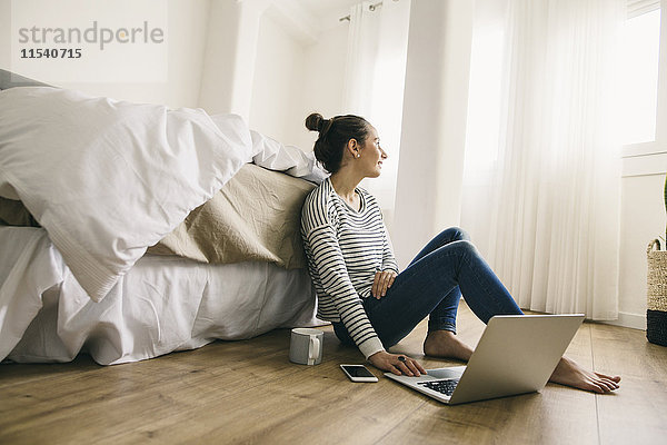 Entspannte Frau sitzt im Schlafzimmer mit Laptop