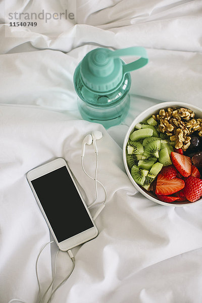 Trinkflasche  Obstschale und Smartphone mit Kopfhörer auf Decke