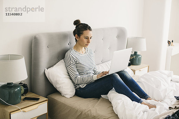 Frau im Bett sitzend mit Laptop