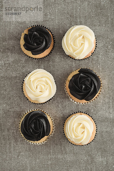 Sechs Tassen Kuchen mit schwarzer und cremefarbener Buttercremeauflage