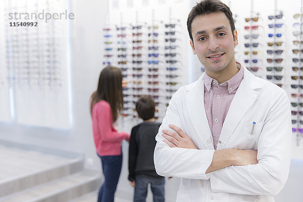 Porträt eines lächelnden Optikers im Geschäft mit Menschen im Hintergrund