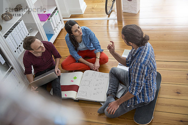 Drei kreative Geschäftsleute  die auf dem Boden sitzen und diskutieren