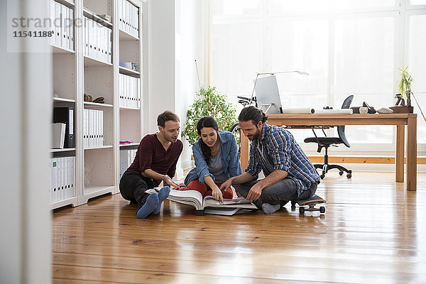 Drei kreative Geschäftsleute sitzen auf dem Boden und schauen in einer Mappe.