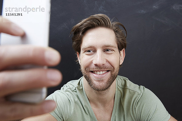 Porträt eines lächelnden jungen Mannes mit einem Selfie mit Smartphone