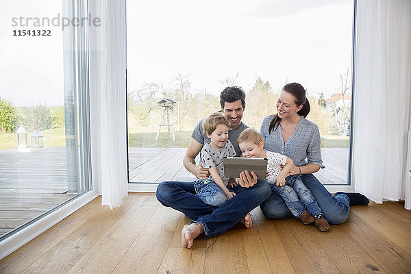 Glückliche Familie auf dem Boden sitzend  mit digitalem Tablett