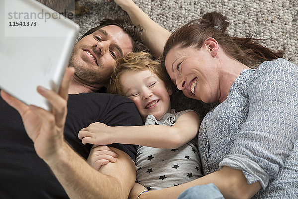 Glückliche Familie auf dem Boden liegend  mit digitalem Tablett