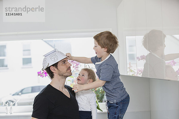 Vater und Söhne spielen zu Hause  mit Sieb als Hut