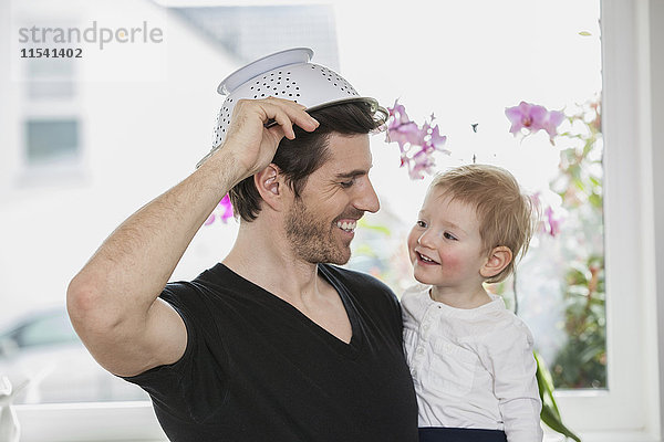 Vater und Sohn spielen zu Hause  mit Sieb als Hut