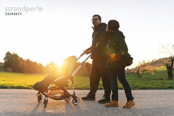 Paar auf einem Spaziergang mit ihrem Baby im Kinderwagen bei Sonnenuntergang