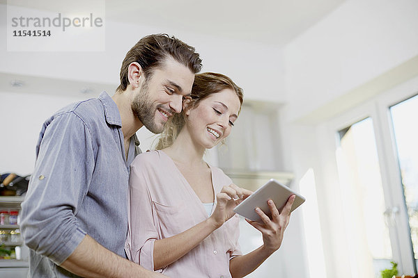 Lächelndes Paar schaut auf digitales Tablett in der Küche