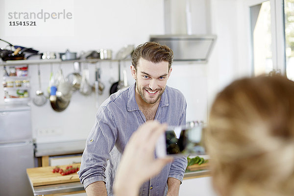 Frau macht Handyfoto von lächelndem Mann in der Küche