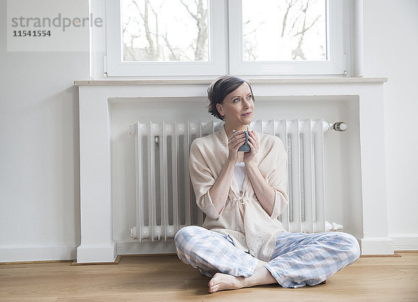 Frau zu Hause auf dem Boden sitzend  Tasse haltend