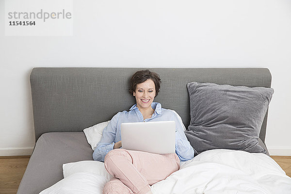 Glückliche Frau auf dem Bett liegend mit Laptop