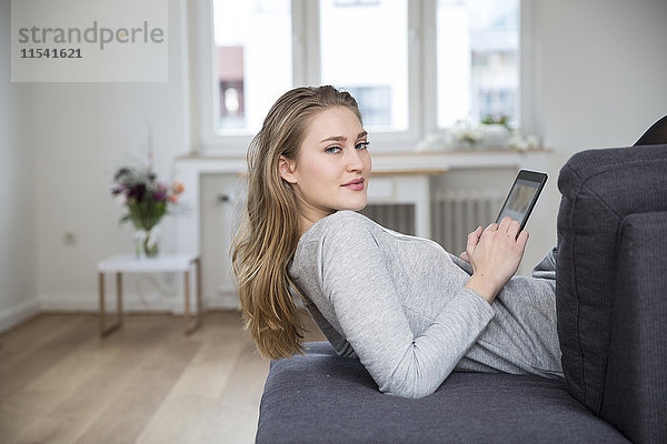 Porträt einer jungen Frau auf der Couch liegend mit digitalem Tablett