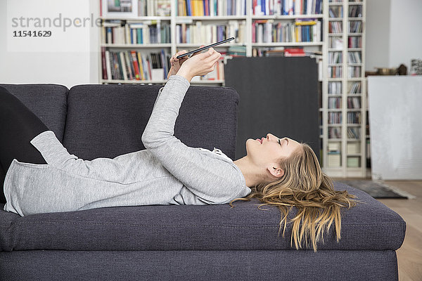 Junge Frau auf der Couch liegend mit digitalem Tablett